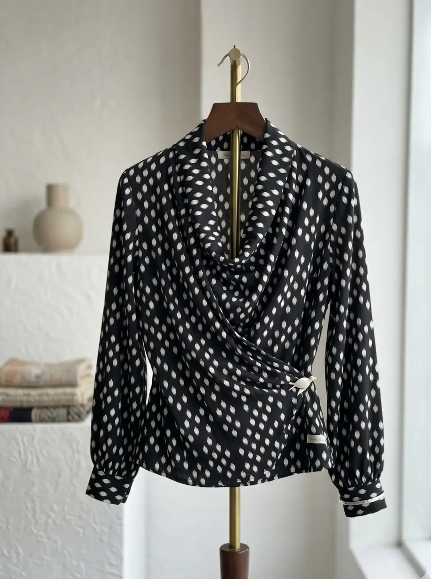 Elegante schwarz-weiße Wickelbluse aus Viskose-Mix mit Ikat-Muster auf einem Kleiderbügel präsentiert.