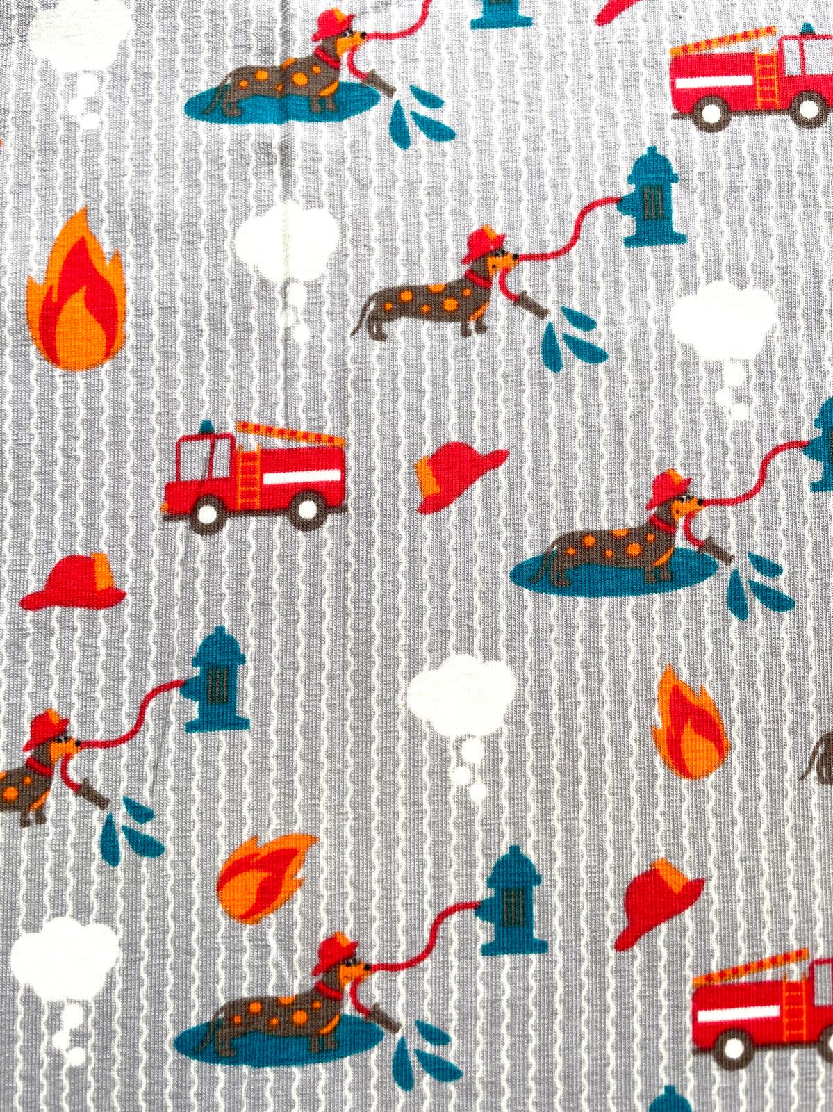 Detailaufnahme eines grau-weiß gestreiften Baumwolljerseys mit bunten Motiven: Dackel mit Feuerwehrhelmen, rote Feuerwehrautos und blaue Hydranten.