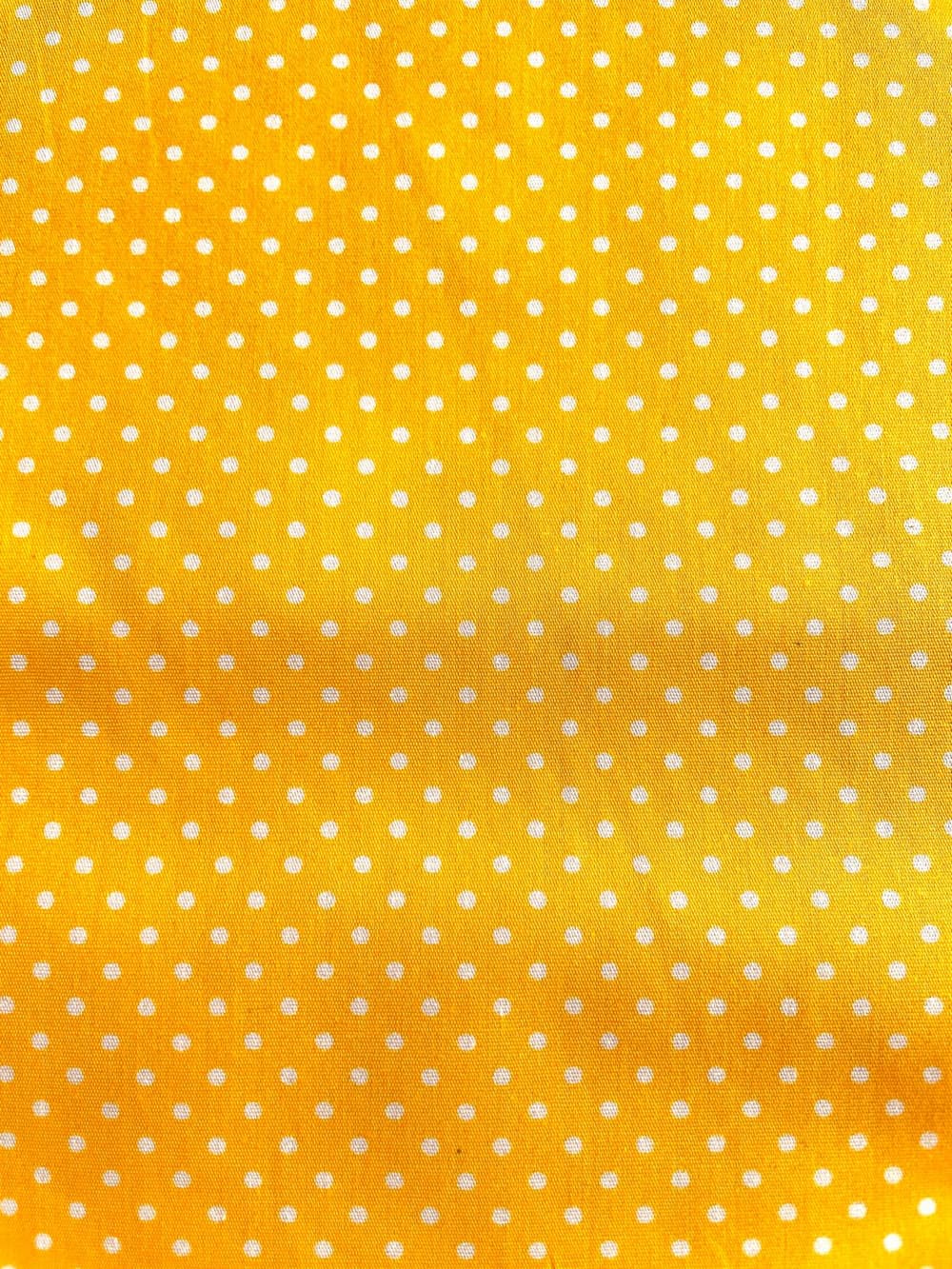 Sonnengelber Baumwollstoff mit regelmäßigem Muster aus kleinen weißen Punkten, blickdichte Webware für Nähprojekte.