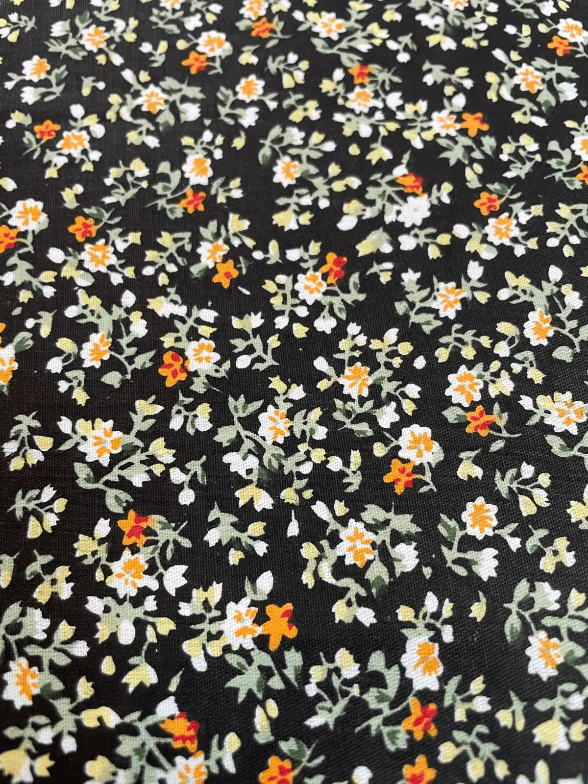 Beschichtete Baumwolle mit kleinen weißen und orangefarbenen Blüten, Millefleurs-Design auf dunklem Hintergrund, abwaschbare Meterware.