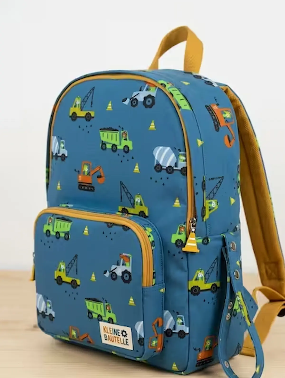 Robuster Baumwollstoff als Webware Meterware in Petrolblau mit bunten Baustellen-Motiven wie Baggern, Lastern und Betonmischern, verarbeitet als fertiger Kinderrucksack auf einer Holzoberfläche.