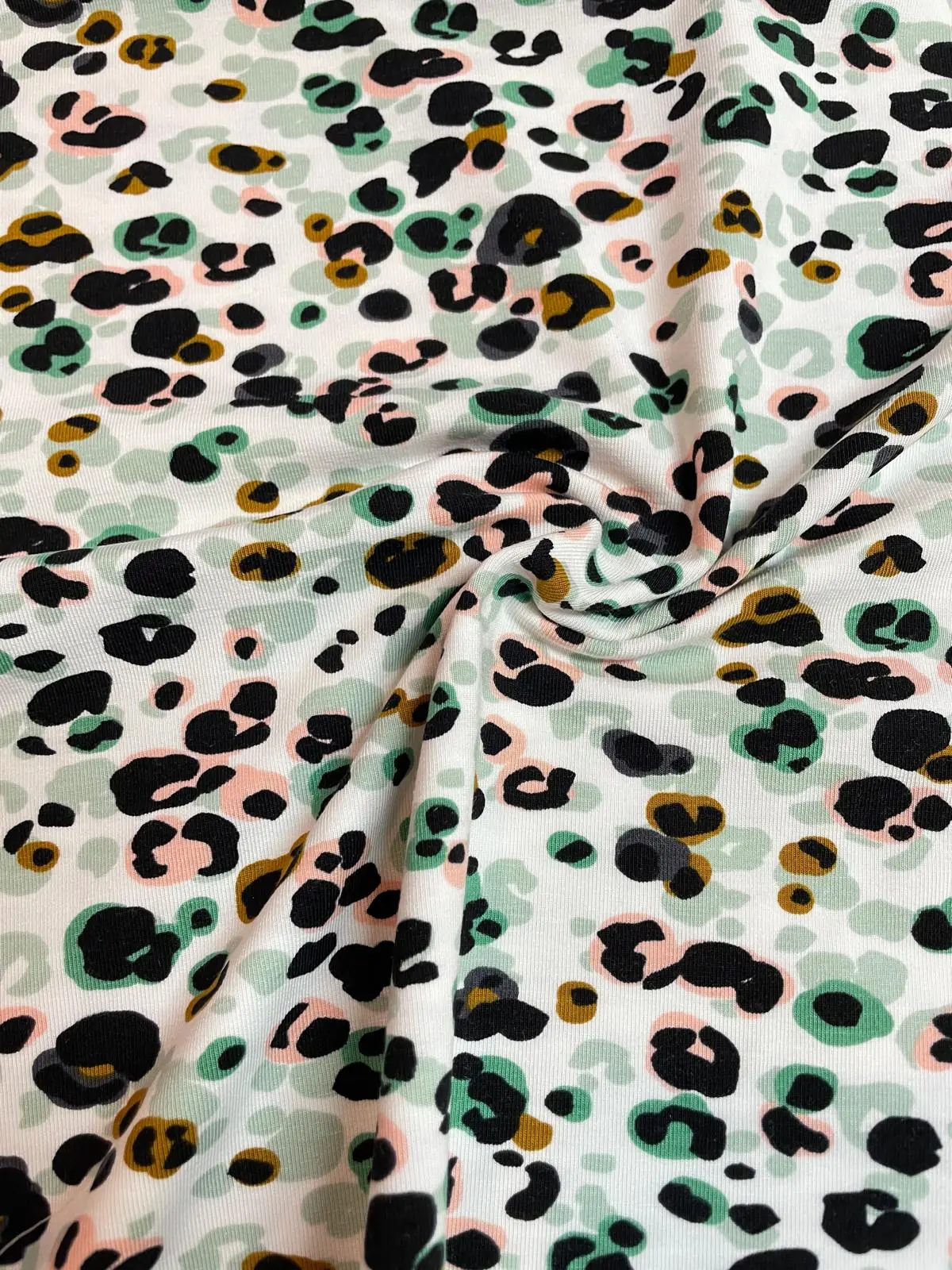 Nahaufnahme von drapiertem Modal-Jersey Stoff mit buntem Leoparden-Print. Die weichen Falten verdeutlichen den fließenden Fall und die seidige Textur des Materials in Grün, Rosa und Ocker auf weißem Grund.