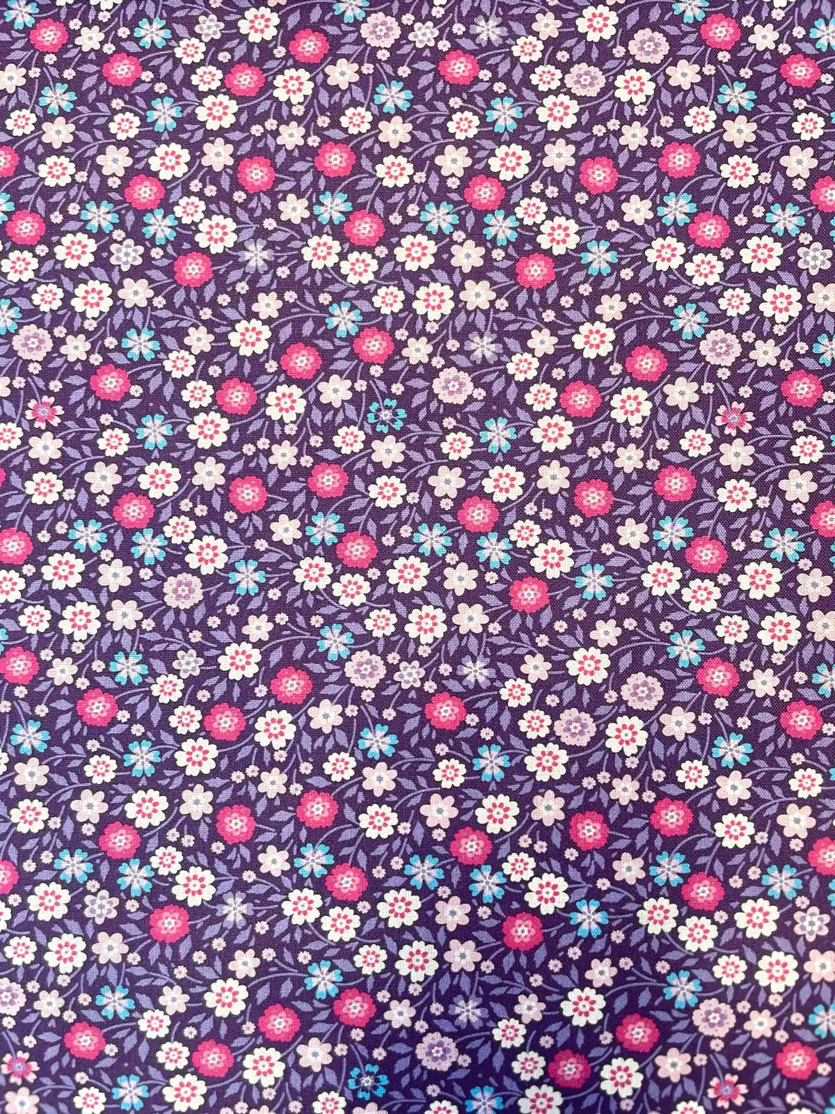 Nahaufnahme einer violetten Baumwoll-Webware mit einem dichten Muster aus kleinen rosa, pinken und hellblauen Streublumen und feinen Blattranken.