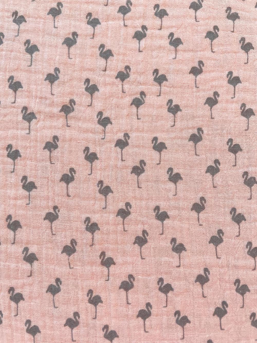 Nahaufnahme von rosa Musselin-Gewebe aus Baumwolle, bedruckt mit kleinen, grauen Flamingo-Silhouetten.