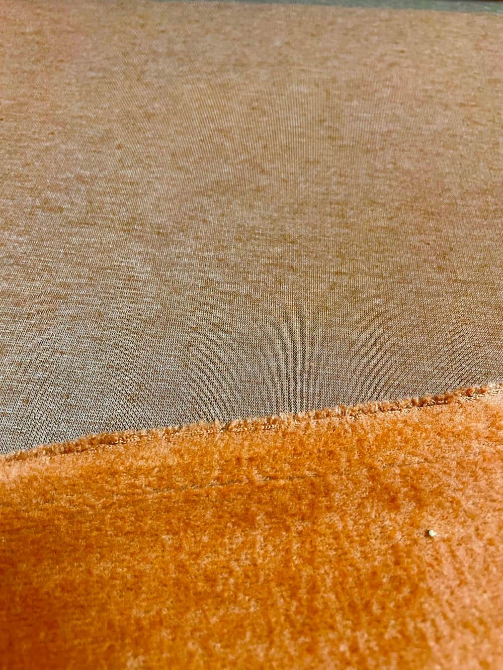 Nahaufnahme von Alpenfleece-Stoff als Meterware in Orange mit glatter, melierter Vorderseite und kuschelig weicher Abseite