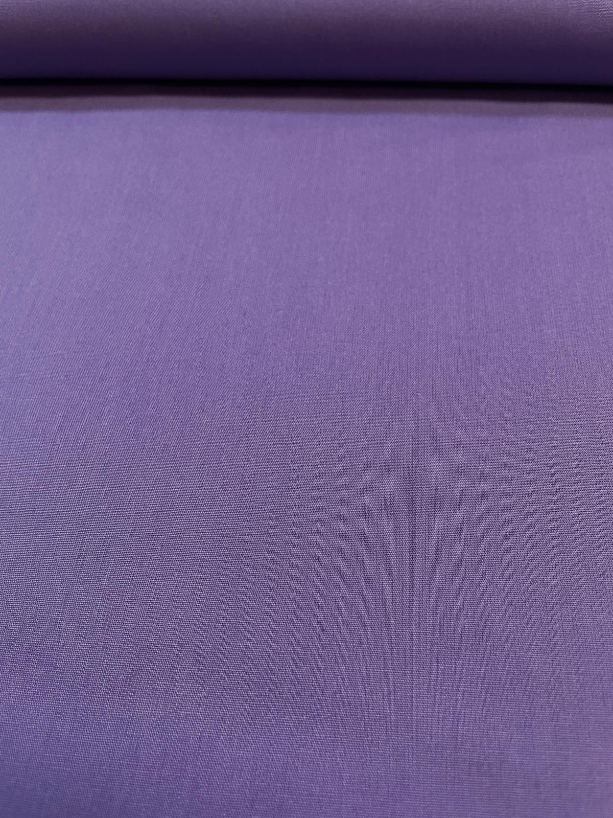 Glatt präsentierter, unelastischer Baumwoll-Popeline Stoff als Meterware in kräftigem Violett, der am oberen Rand ordentlich über eine Stoffrolle liegt und eine feine, dichte Webstruktur zeigt.