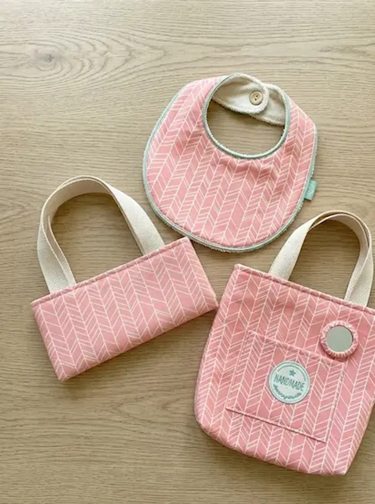 Handgenähtes Baby-Set aus rosa Baumwollstoff mit weißem Fischgrätenmuster: Lätzchen und kleine Henkeltaschen mit Handmade-Label