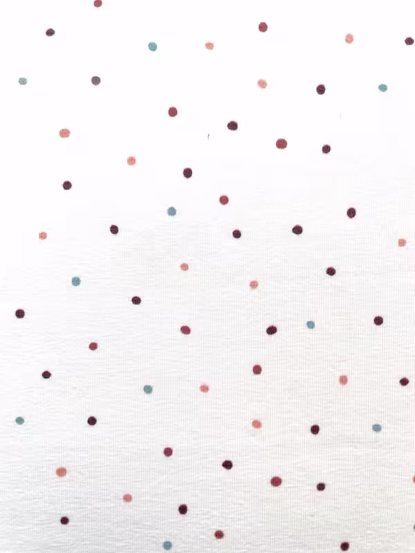Weißer Jersey-Stoff aus Baumwolle mit kleinen, unregelmäßig verteilten Punkten in den Farben Terrakotta, Salbeigrün, Altrosa und Dunkelrot.