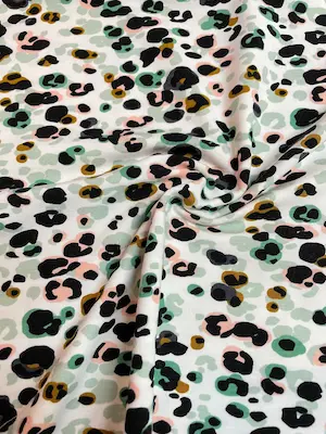 Nahaufnahme von drapiertem Modal-Jersey Stoff mit buntem Leoparden-Print. Die weichen Falten verdeutlichen den fließenden Fall und die seidige Textur des Materials in Grün, Rosa und Ocker auf weißem Grund.