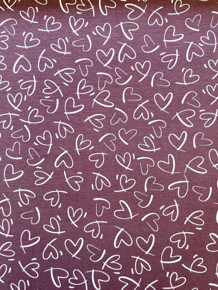 Hochwertiger violetter Jerseystoff mit weißem, handgezeichnetem Herzmuster, Meterware aus 95% Baumwolle für Damen- und Kinderbekleidung.
