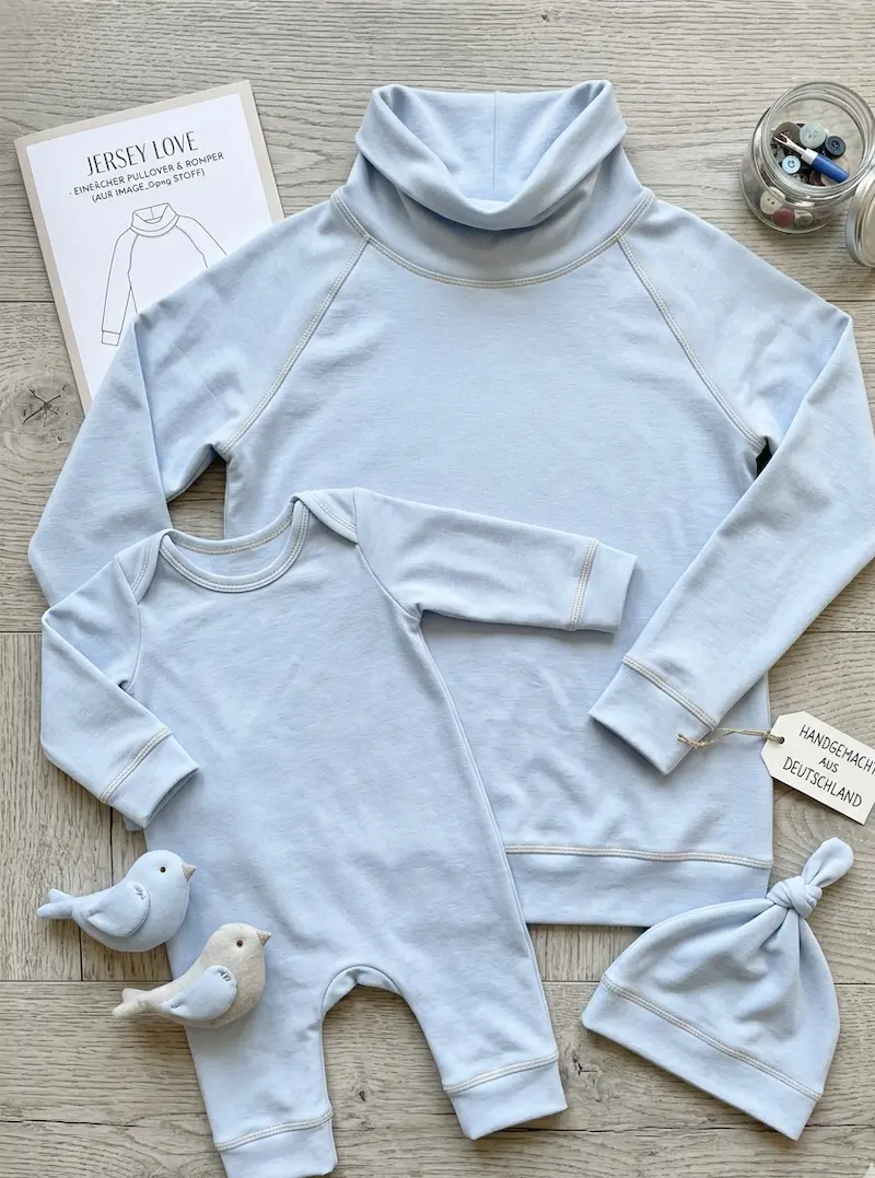 Hellblaues Baby-Set bestehend aus Pullover, Romper und Mütze aus Baumwolljersey Uni Meterware, flach liegend auf Holzboden mit Schnittmuster.