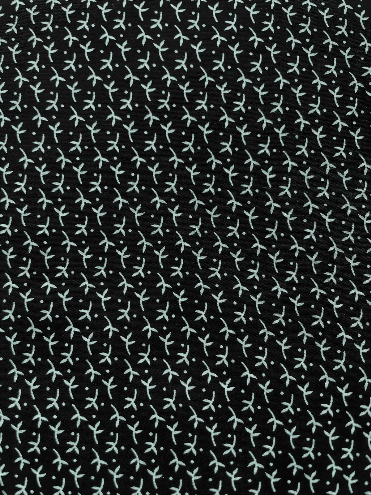 Minimalistisches Muster aus kleinen weißen Blättern und Punkten auf tiefschwarzem Viskosestoff. Die Nahaufnahme zeigt das gleichmäßige, grafische Design und die matte Oberfläche des feinen Gewebes.