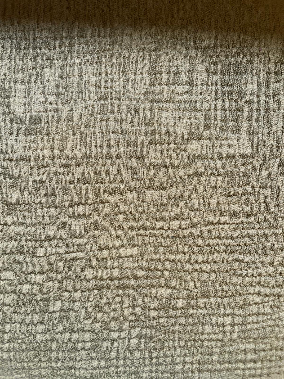 Nahaufnahme von beige-farbenem Musselin-Stoff aus 100% Baumwolle mit charakteristischer Crinkle-Struktur für Babykleidung.