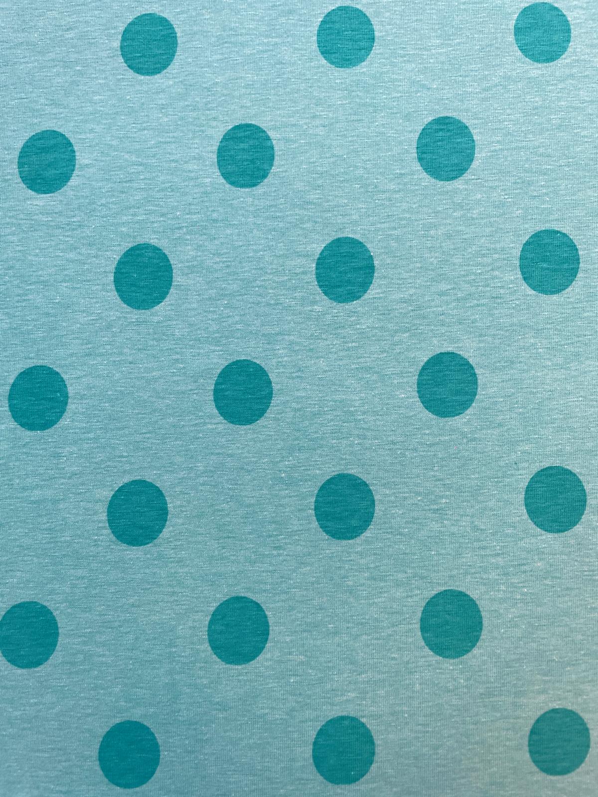 Nahaufnahme eines türkisfarbenen Jerseystoffs mit einem regelmäßigen Muster aus dunkelblauen Punkten (Polka Dots), ideal als elastische Meterware für Kleidung.