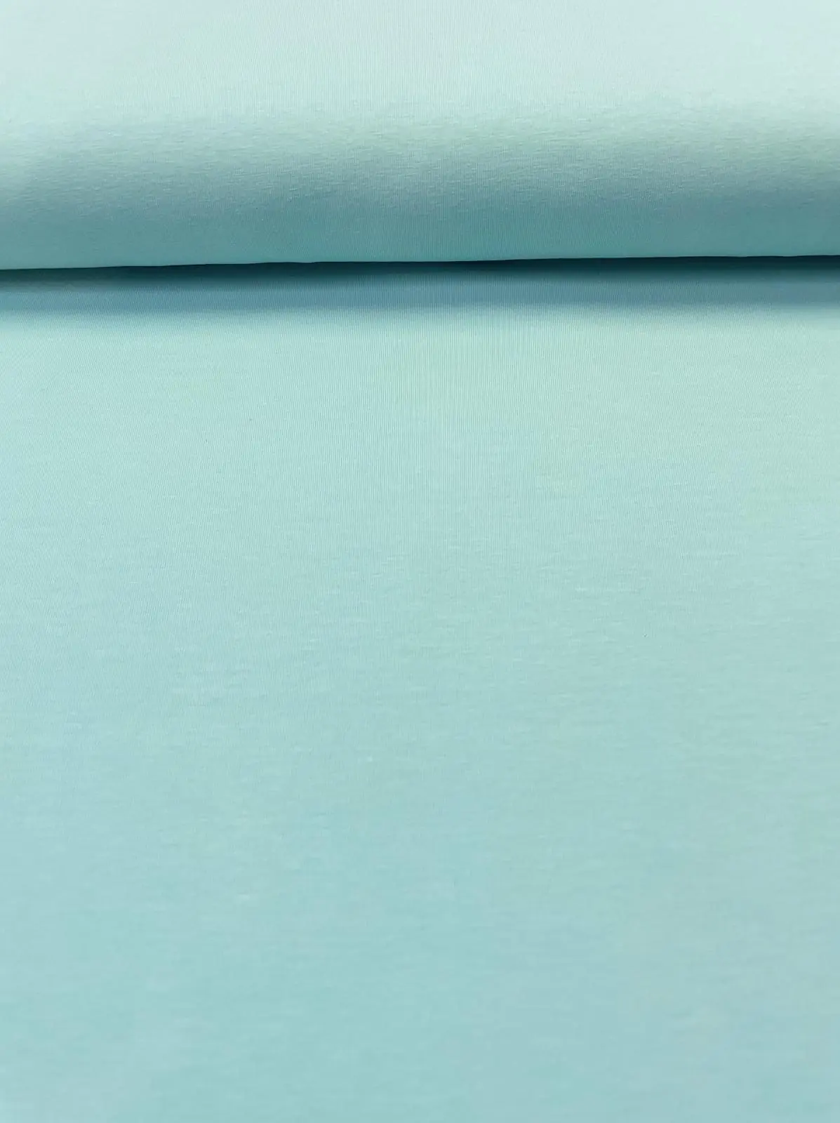 Nahaufnahme eines glatten Jerseystoffs in hellem Mint, elastische Baumwoll-Meterware für Kleidung.