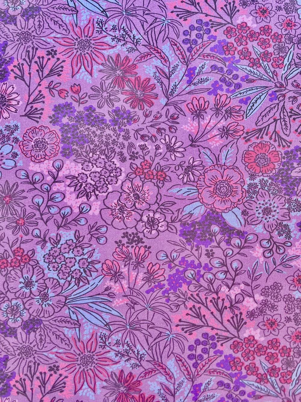 Bunter Baumwoll-Popeline Stoff als Meterware mit verspieltem Blumen-Muster in Lila- und Rosatönen für Kleidung und Dekoration.