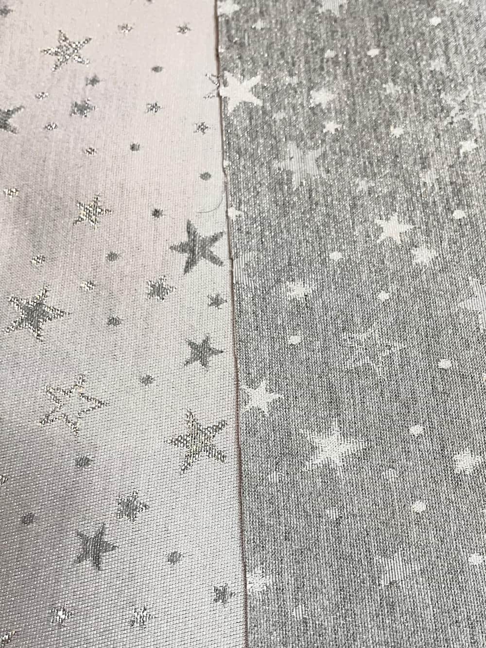 Deko-Stoff in Silber als Meterware, der beide Seiten im direkten Vergleich zeigt – mit glänzenden Sternenmotiven auf heller und dunklerer Hintergrundseite.
