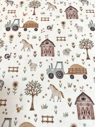 Weißer Jersey-Stoff mit detaillierten Bauernhof-Motiven im Aquarell-Stil: Traktor mit Heuanhänger, Scheune, Pferde, Ziegen, Schafe und Sonnenblumen.