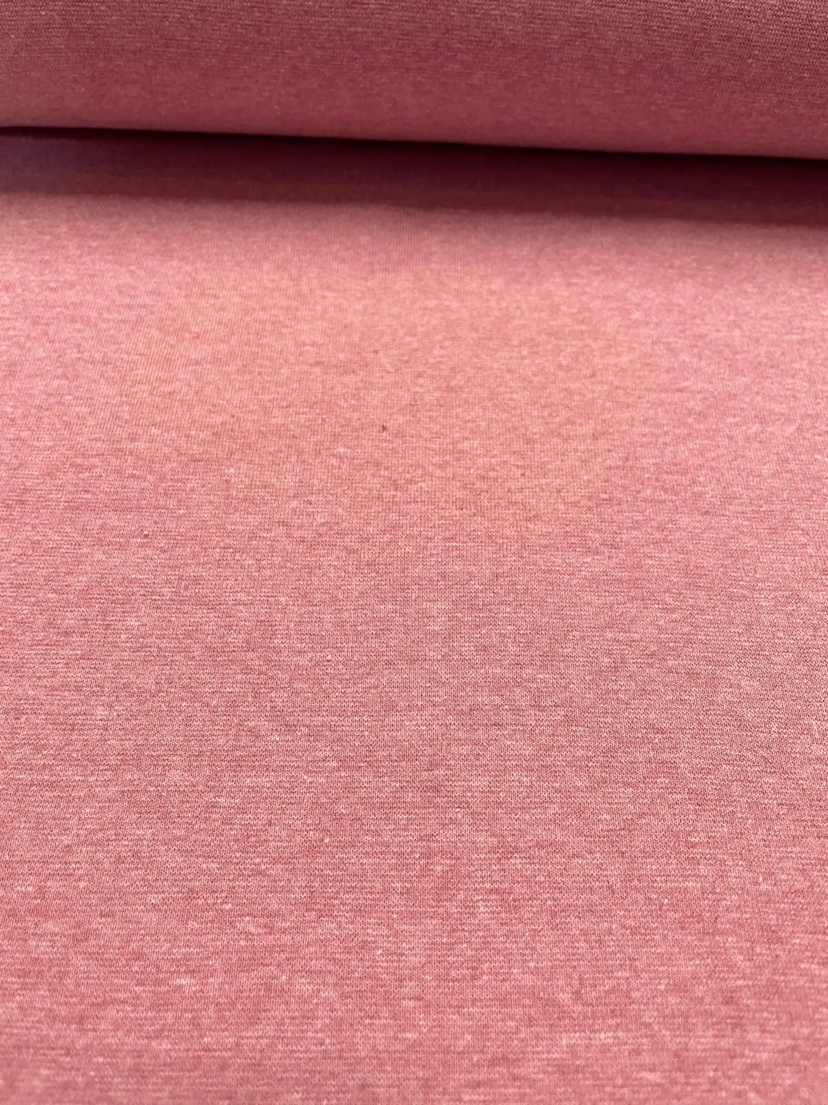 Nahaufnahme von einem elastischen Bündchenstoff in hellem Pinkrosa mit feineNahaufnahme von einem elastischen Bündchenstoff in hellem Pinkrosa mit feiner Melange-Strickstruktur als Meterware für Kleidung.r Melange-Strickstruktur a