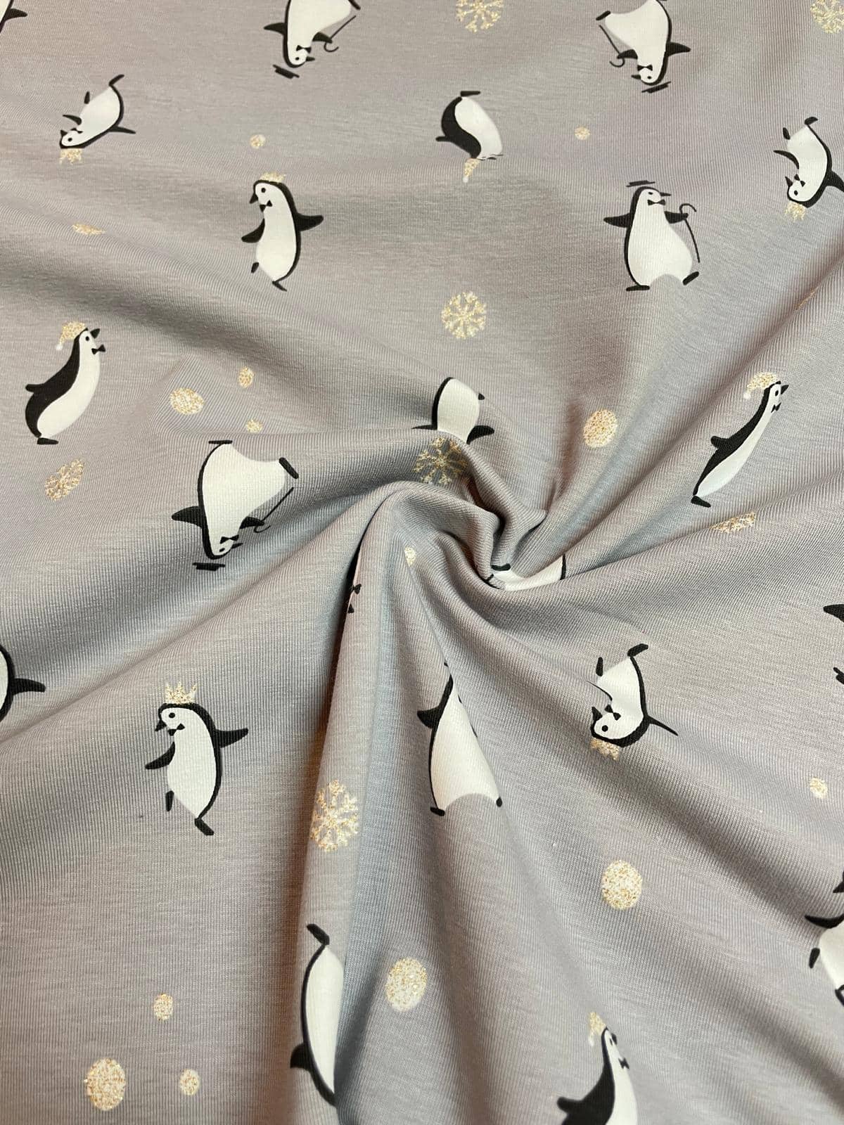 Grauer Baumwoll-Jersey als Meterware mit niedlichen Pinguinen, glitzernden Schneeflocken und goldenen Glitzerpunkten für den Winter