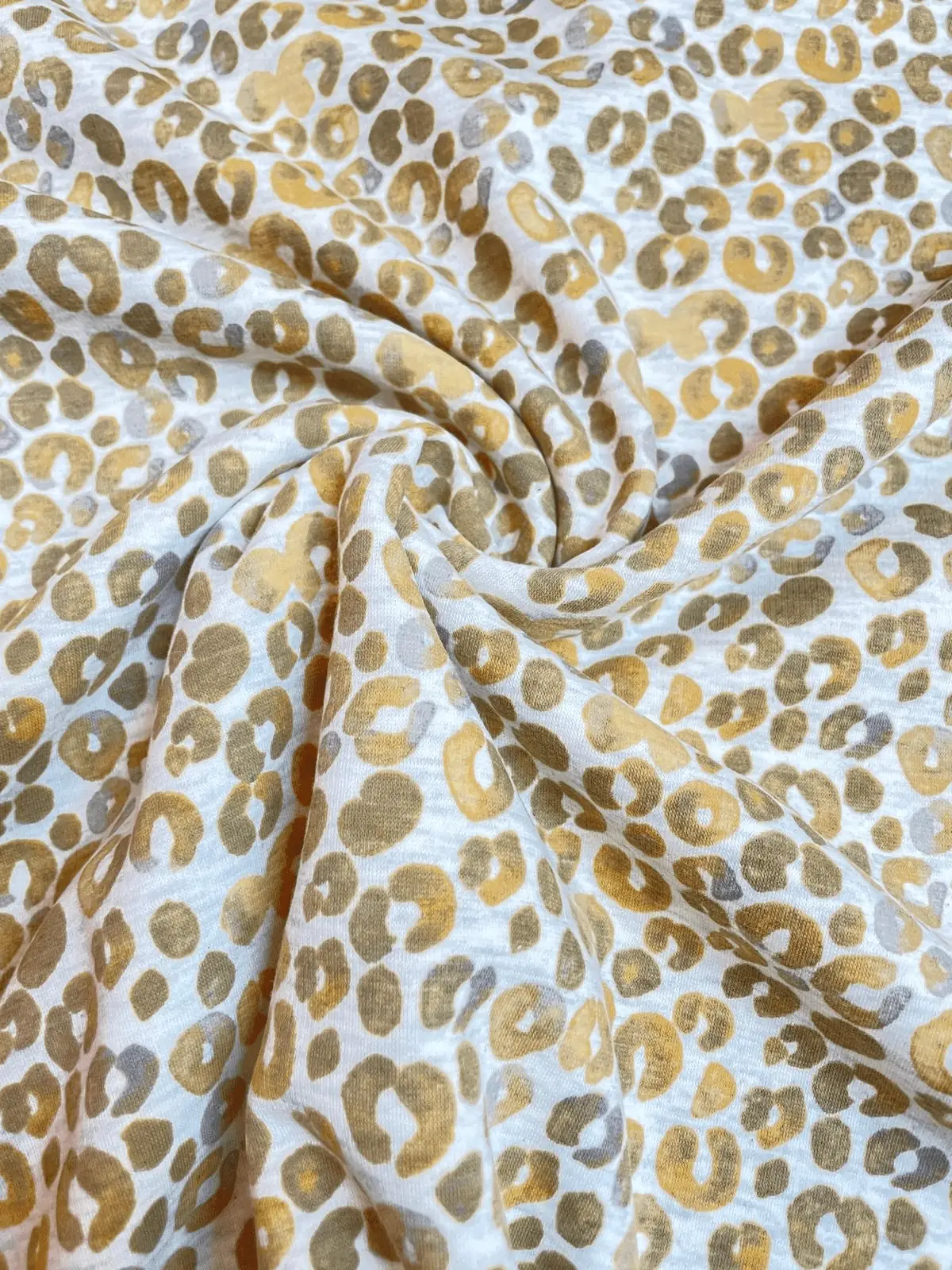 Hochwertiger Alpenfleece-Stoff mit modernem Leoparden-Print in den Farben Beige, Senfgelb und Grau. Der Stoff liegt in weichen Falten und zeigt eine feine Strickoberfläche.