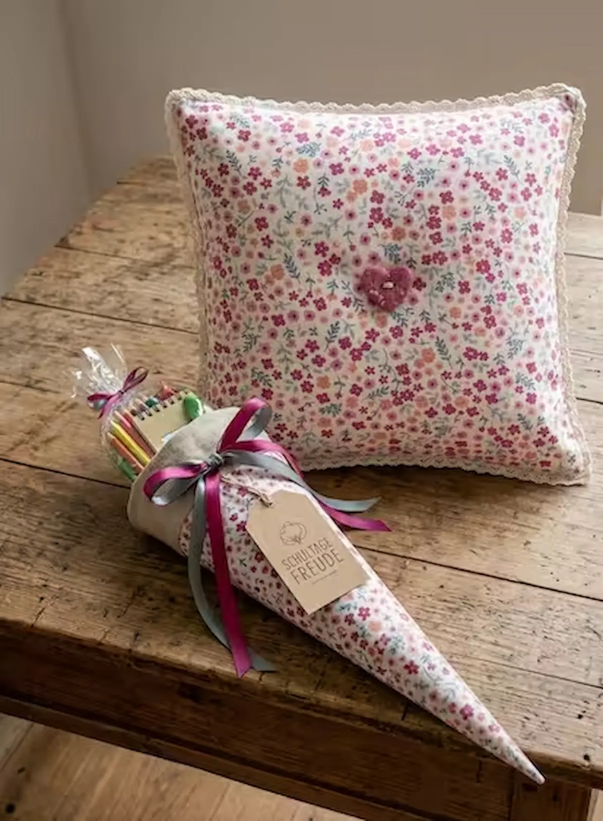 Feiner Baumwollstoff als Webware Meterware mit buntem Streublumenmuster in Pink, Rosa und Orange, verarbeitet als handgenähte Schultüte zur Einschulung und passendes Dekokissen auf einem Holztiertisch.