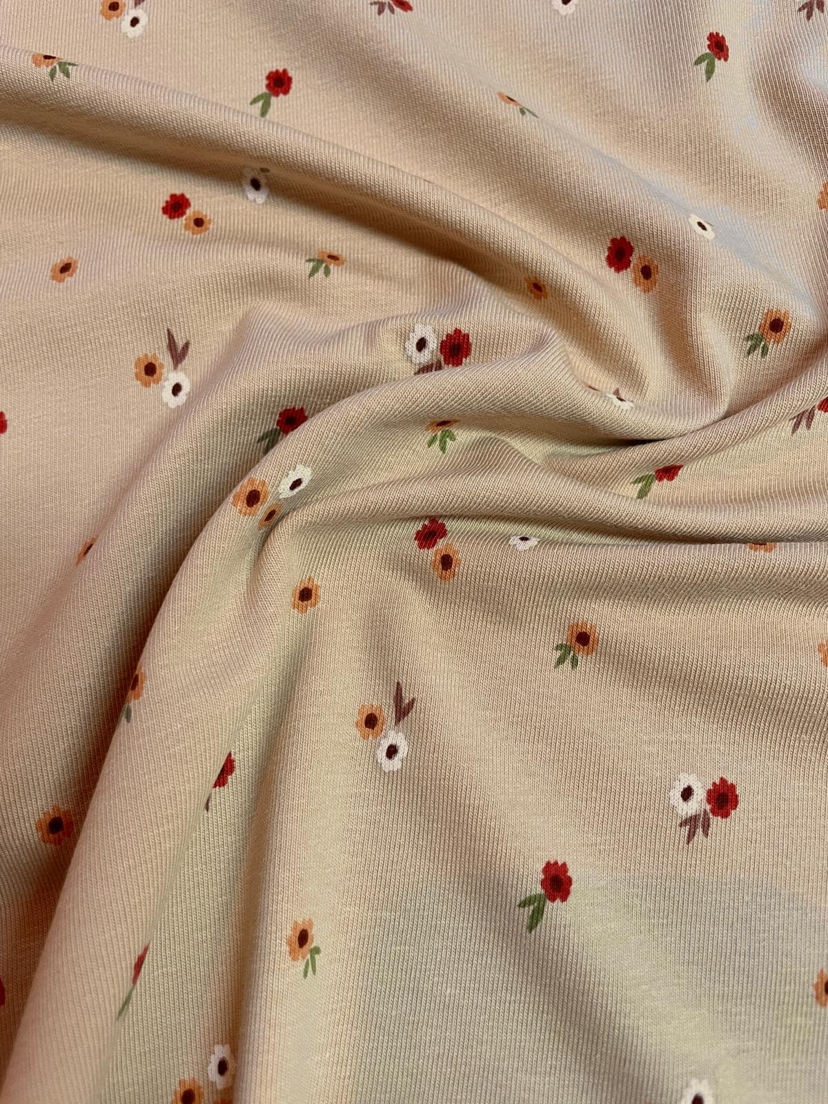 Weicher Jerseystoff in Beige mit kleinen roten und orangen Streublumen, elastische Baumwoll-Meterware für Kinderkleidung und Baby-Accessoires.