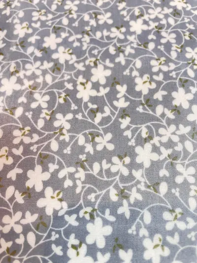 Beschichteter Baumwollstoff in Grau mit filigranen weißen Blumenranken und dezenten olivgrünen Blättern.