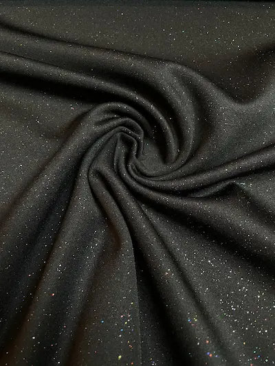 Nahaufnahme eines schwarzen Jerseystoffs, der mit vielen kleinen, bunten Glitzerpunkten (Multicolor) übersät ist und im Licht funkelt.