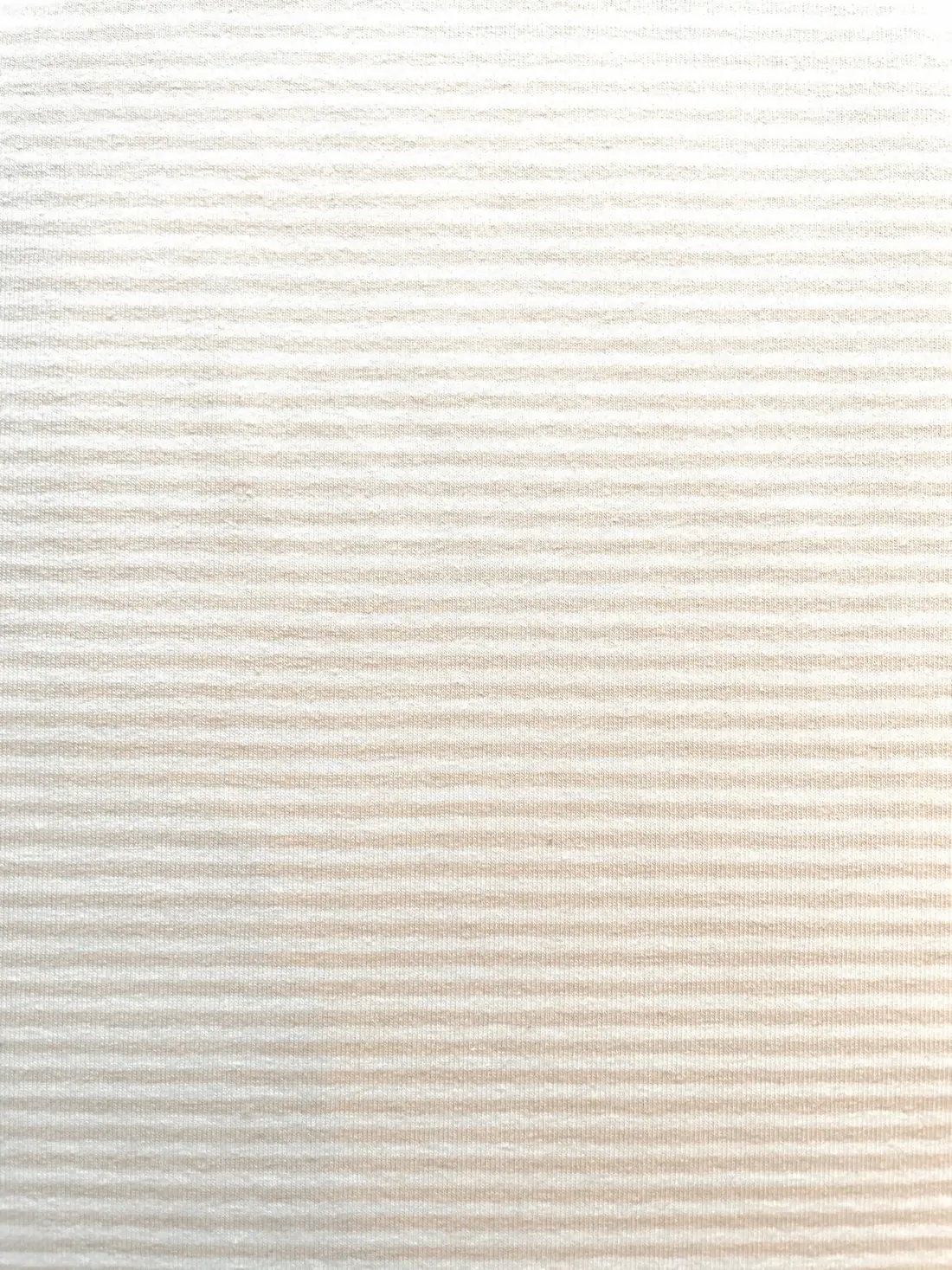 Nahaufnahme von weichem Baumwolljersey in Beige-Creme mit sehr feinen weißen Nadelstreifen, hochwertige Meterware für dezente Baby- und Damenbekleidung.