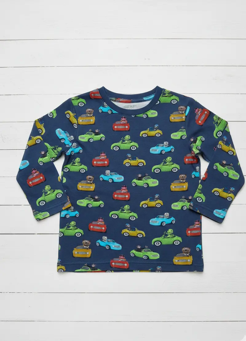 Ein dunkelblaues Langarmshirt für Kinder mit einem bunten Allover-Print aus verschiedenen Autos in Rot, Gelb, Grün und Blau. Das Shirt liegt flach auf einem weißen Holzhintergrund und zeigt das lebendige Fahrzeug-Motiv des Baumwolljerseys.