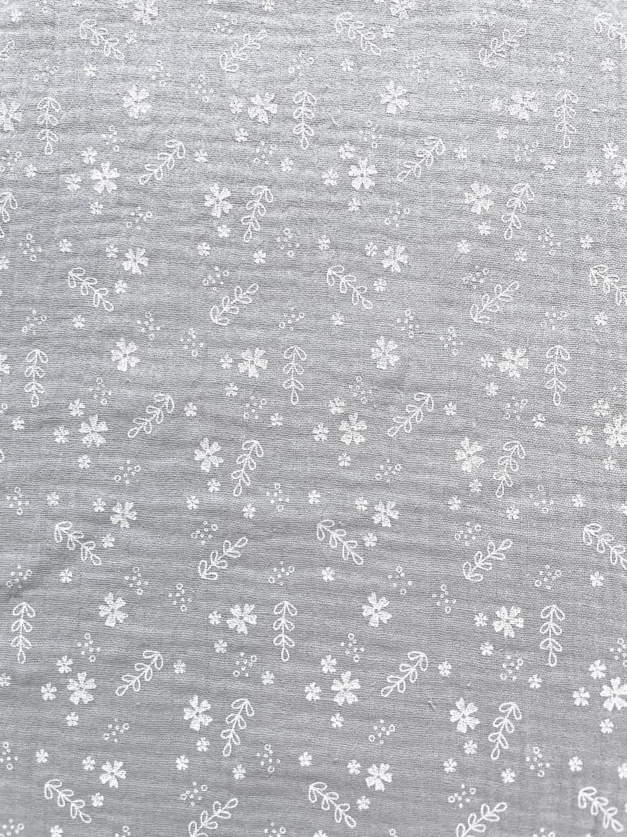 Hellgrauer Musselin-Stoff aus reiner Baumwolle mit feinen weißen Blüten und Zweigen, weiche Crinkle-Struktur für Bekleidung.