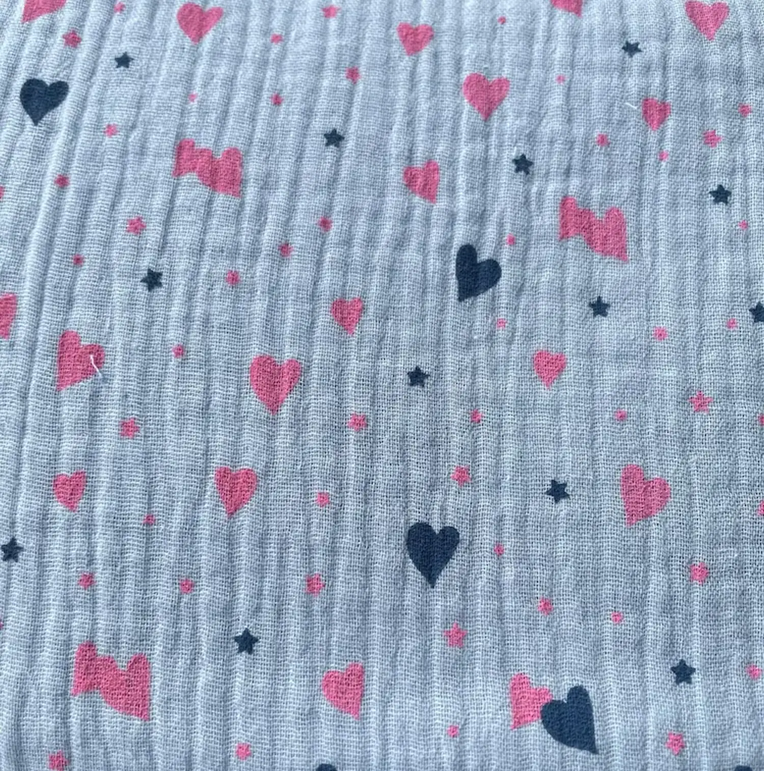 Weicher Musselin-Stoff in hellem Graublau, bedruckt mit rosa Herzen und dunkelblauen Sternen. Klassische Double-Gauze Baumwollqualität mit Crinkle-Optik für Kinderzimmer-Deko und Kleidung