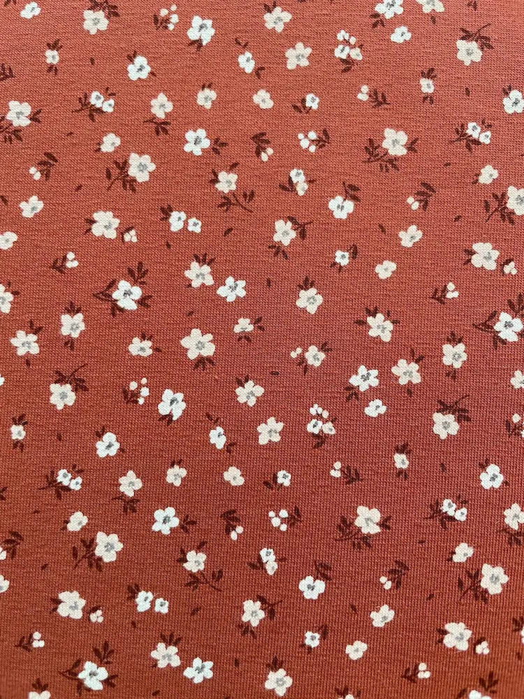 Weicher Jerseystoff in Rostbraun mit zierlichem weißen Blumenmuster, ideal für Kinderkleidung und Damenmode
