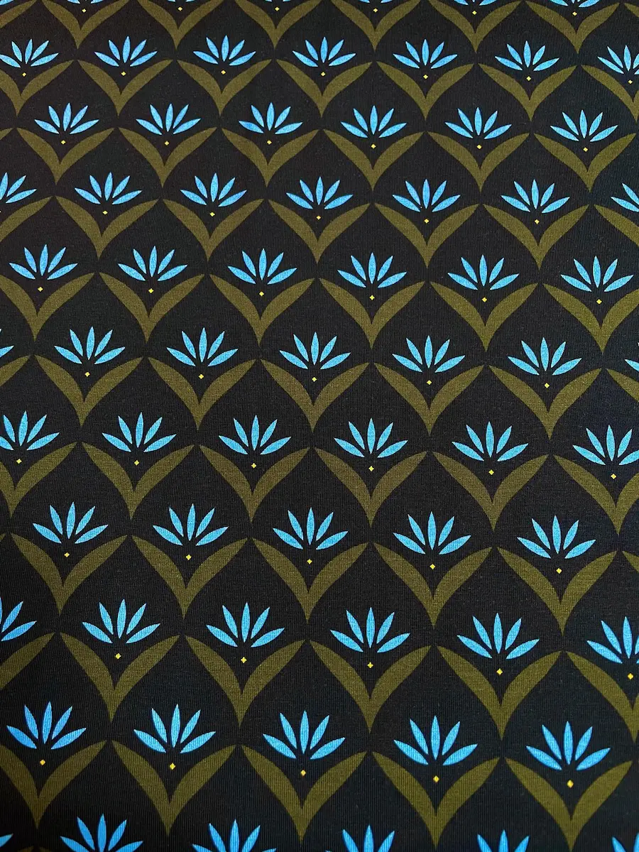 Nahaufnahme eines elastischen Jersey-Stoffs mit einem stilisierten floralen Retro-Muster. Hellblaue Blütenblätter in olivgrünen Fassungen bilden ein geometrisches Rapport-Muster auf dunklem Grund.