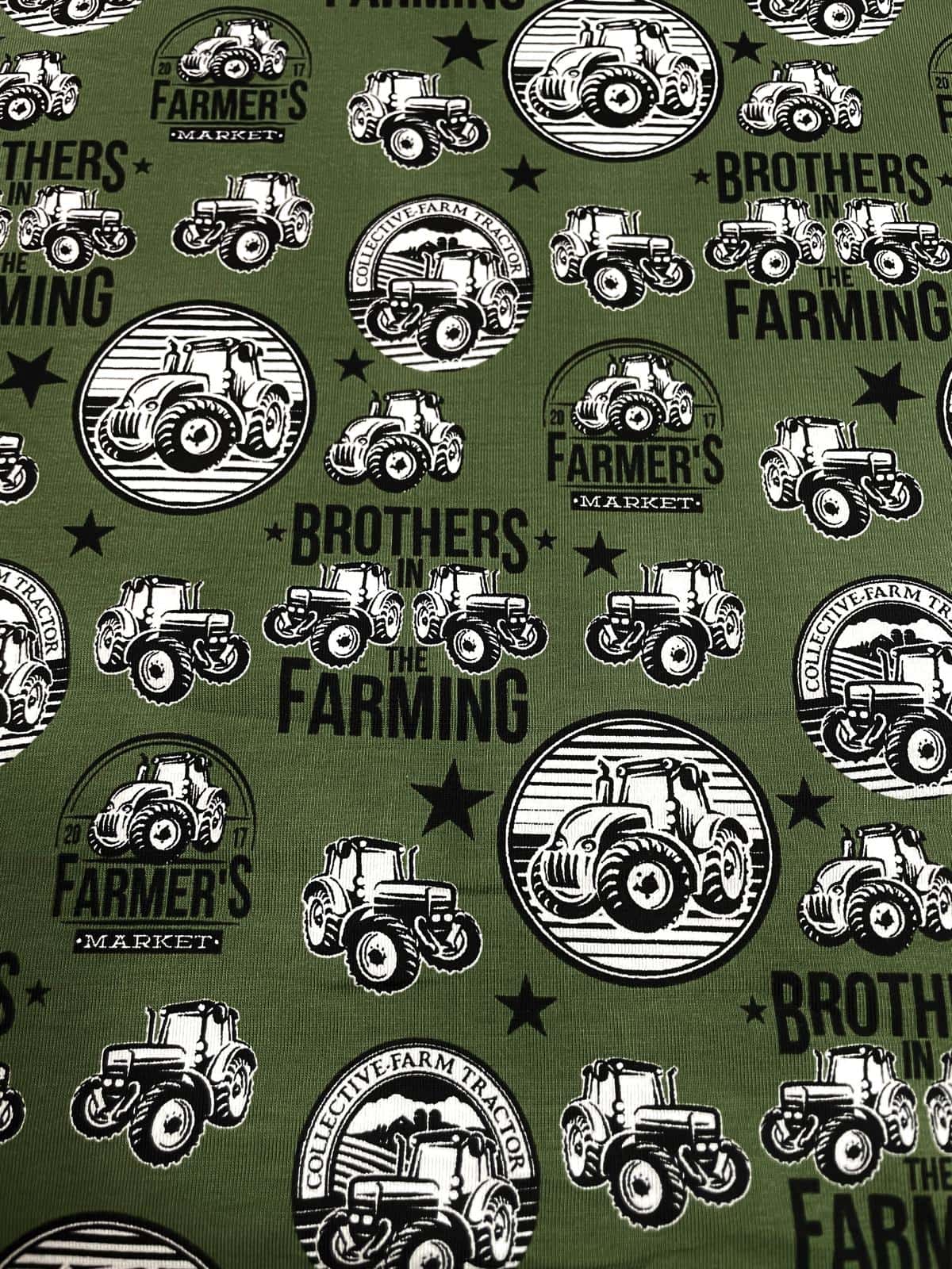 Olivgrüner Baumwolljersey-Stoff als Meterware, flach fotografiert und bedruckt mit einem coolen Vintage-Muster aus schwarz-weißen Traktoren, Sternen und Logos wie "Brothers in Farming" und "Farmer's Market".