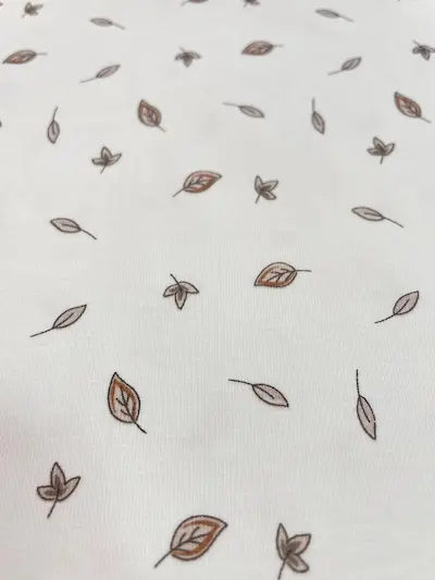 Hochwertiger weißer Jerseystoff mit kleinen, dezenten Blättern in Braun und Beige, minimalistisches Design für Babykleidung und moderne Basics.