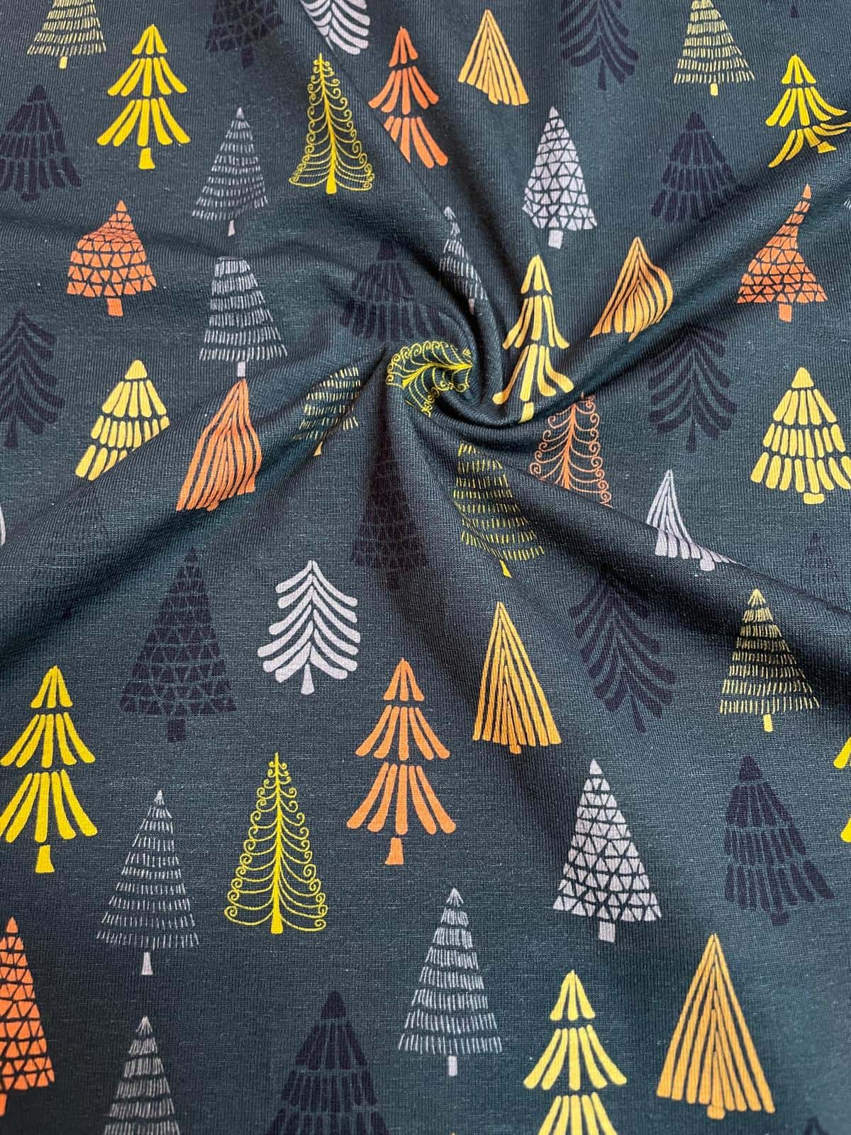 Anthrazitfarbener Jersey-Stoff als Meterware mit einem Muster aus stilisierten Tannenbäumen in Gelb, Orange, Weiß und Grau für Winter und Weihnachten.Dunkelgrüner Jersey-Stoff als Meterware mit einem Muster aus stilisierten Tannenbäumen in Gelb, Orange, W