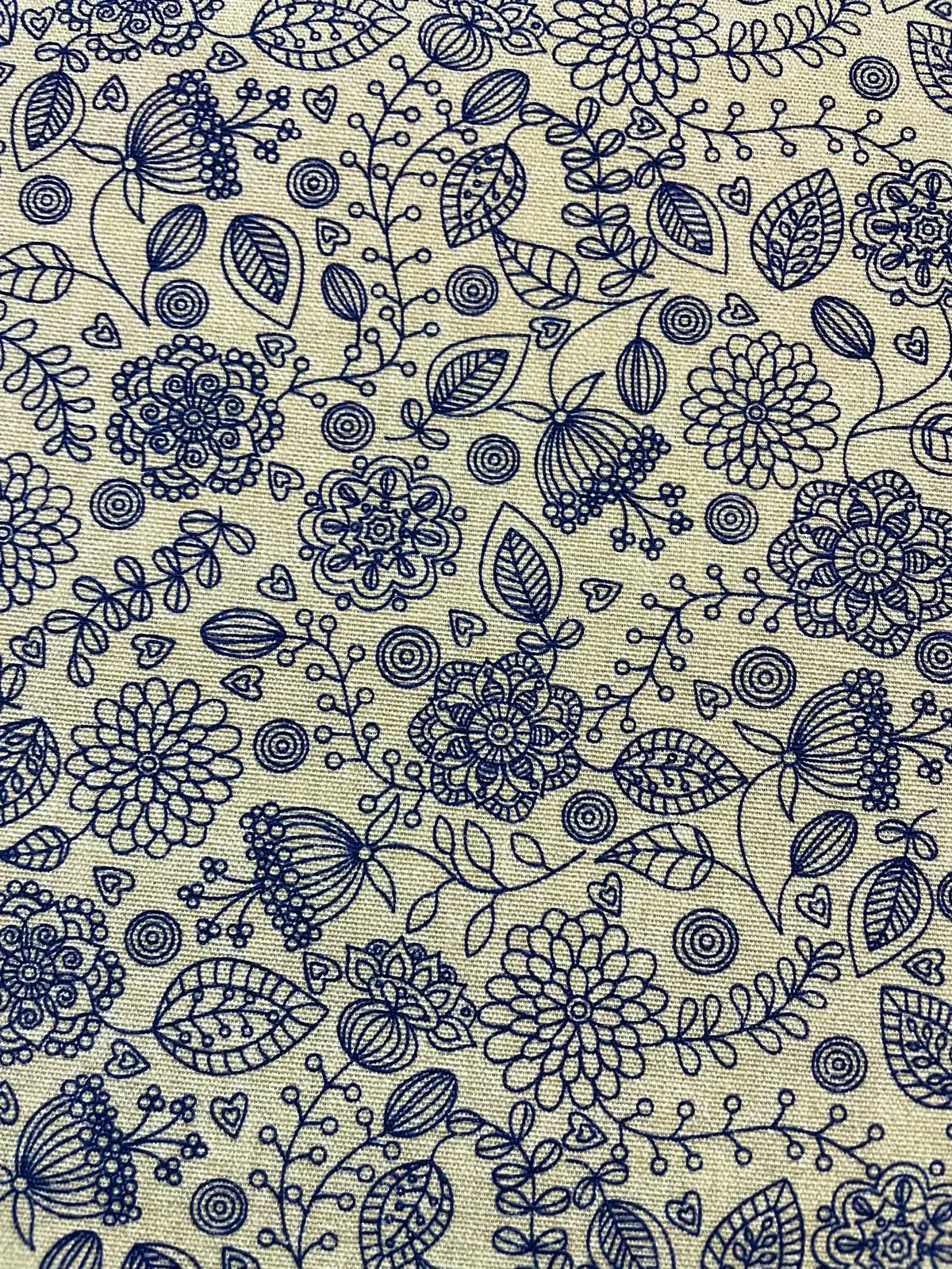 Strukturierter Canvas Dekostoff als Meterware in Natur-Beige mit einem feinen, dunkelblauen Linienmuster aus Blumen, Ranken und kleinen Herzen.