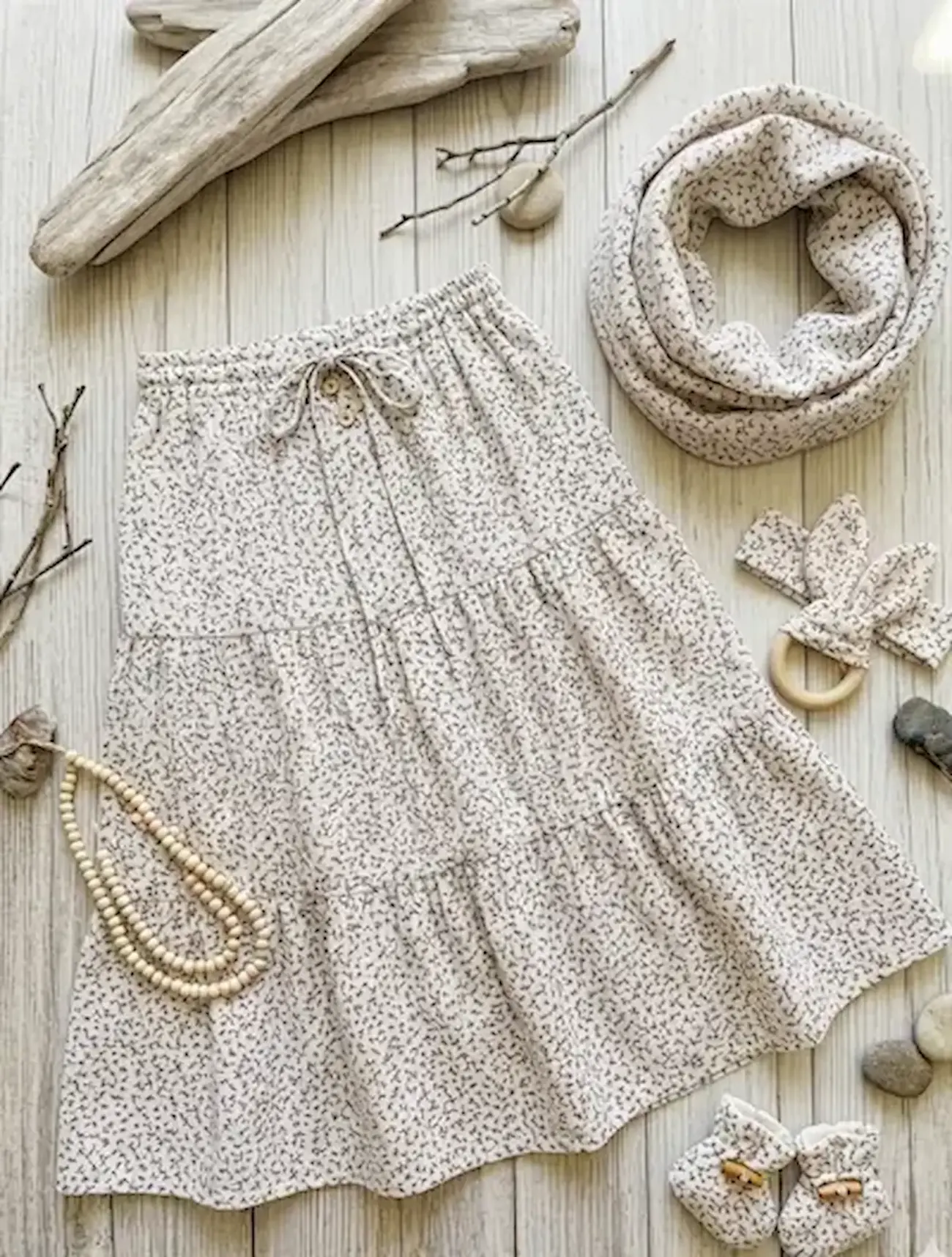 Grau-weiß-schwarz gemusterter Musselin-Stoff als Meterware, flach liegend dekoriert als Set aus Kinder-Stufenrock, Loop-Schal, Stirnband und Babyschuhen in modernem Flatlay-Design.