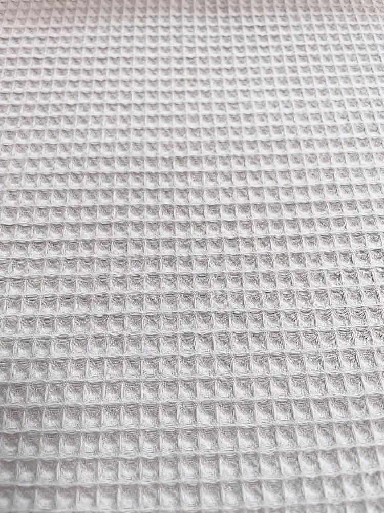 Nahaufnahme von hellgrauem Waffelpique Stoff als Meterware mit feiner Waffelstruktur für Bademäntel, Handtücher und Baby-Zubehör.
