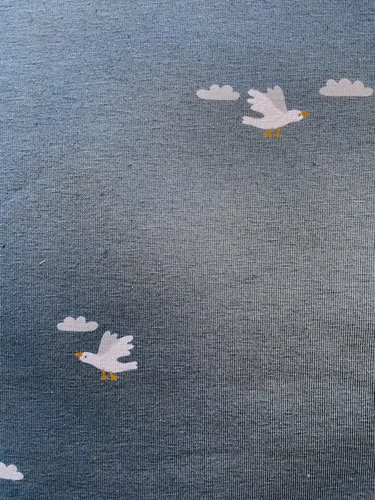 Detailansicht eines blauen Baumwolljersey-Stoffs mit weißem Möwen-Print; zeigt die glatte, feine Maschenstruktur des Textils.