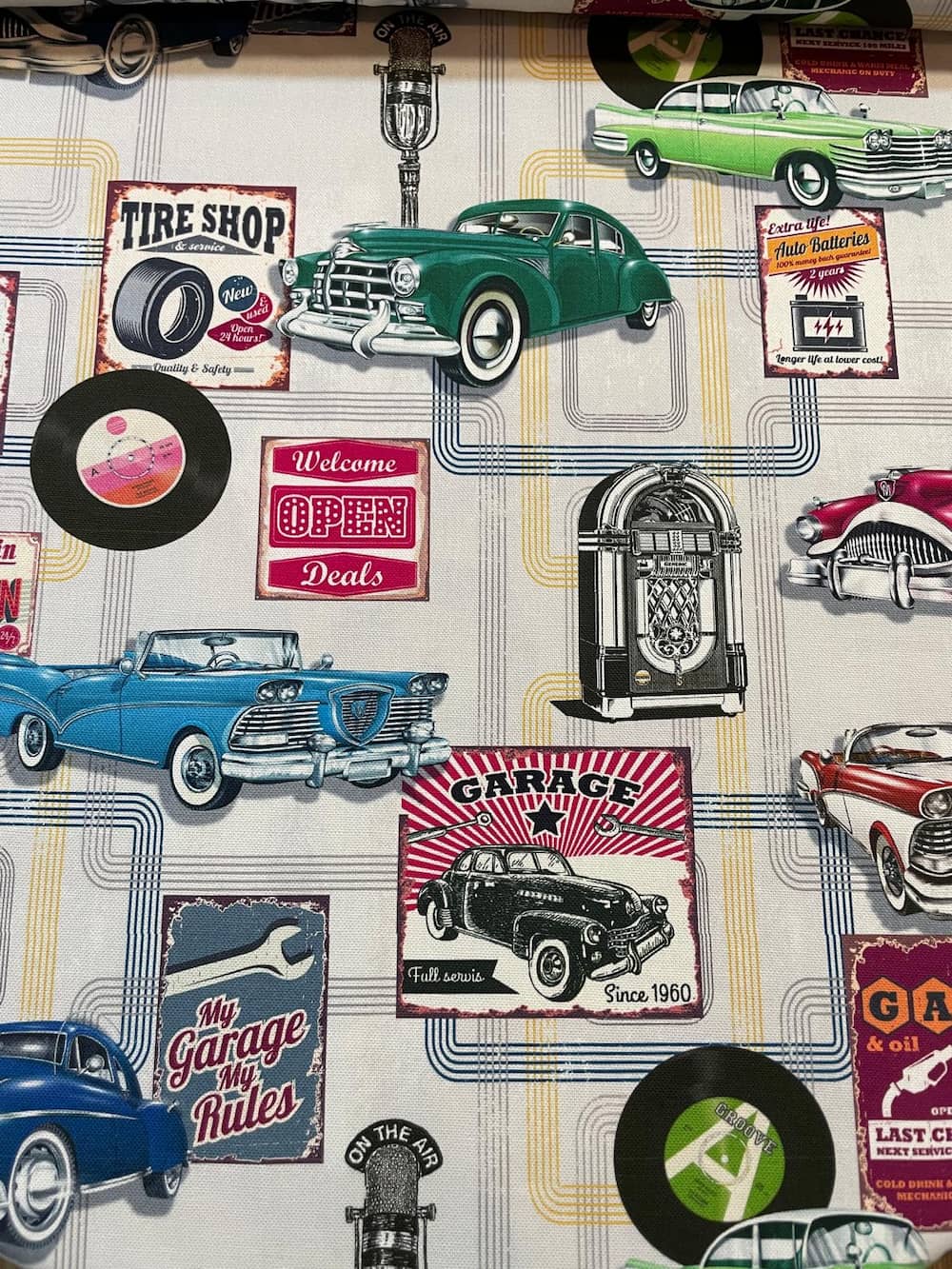 Farbenfroher Dekostoff als Meterware im Vintage-Stil mit klassischen Oldtimern, Jukeboxen, Schallplatten und amerikanischen Werkstatt-Schildern.