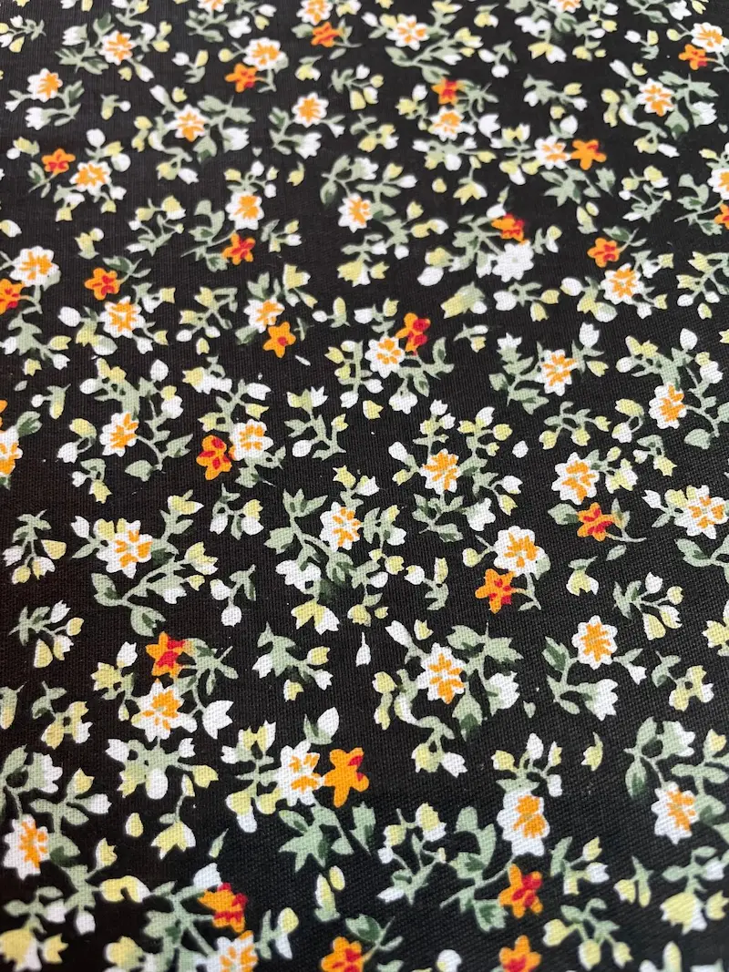 Beschichtete Baumwolle mit kleinen weißen und orangefarbenen Blüten, Millefleurs-Design auf dunklem Hintergrund, abwaschbare Meterware.