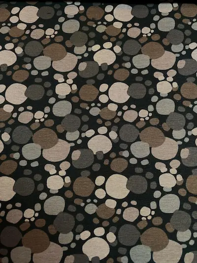 Dunkler Alpenfleece-Stoff mit einem Muster aus abstrakten Pfotenabdrücken und Punkten in verschiedenen Erdtönen wie Braun, Taupe, Beige und Grau auf schwarzem Hintergrund.