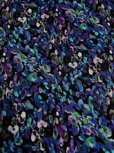 Dunkler Alpenfleece-Stoff mit einem dichten, abstrakten Muster aus organischen Punkten und Flecken in leuchtendem Blau, Violett, Smaragdgrün und Weiß auf schwarzem Grund.