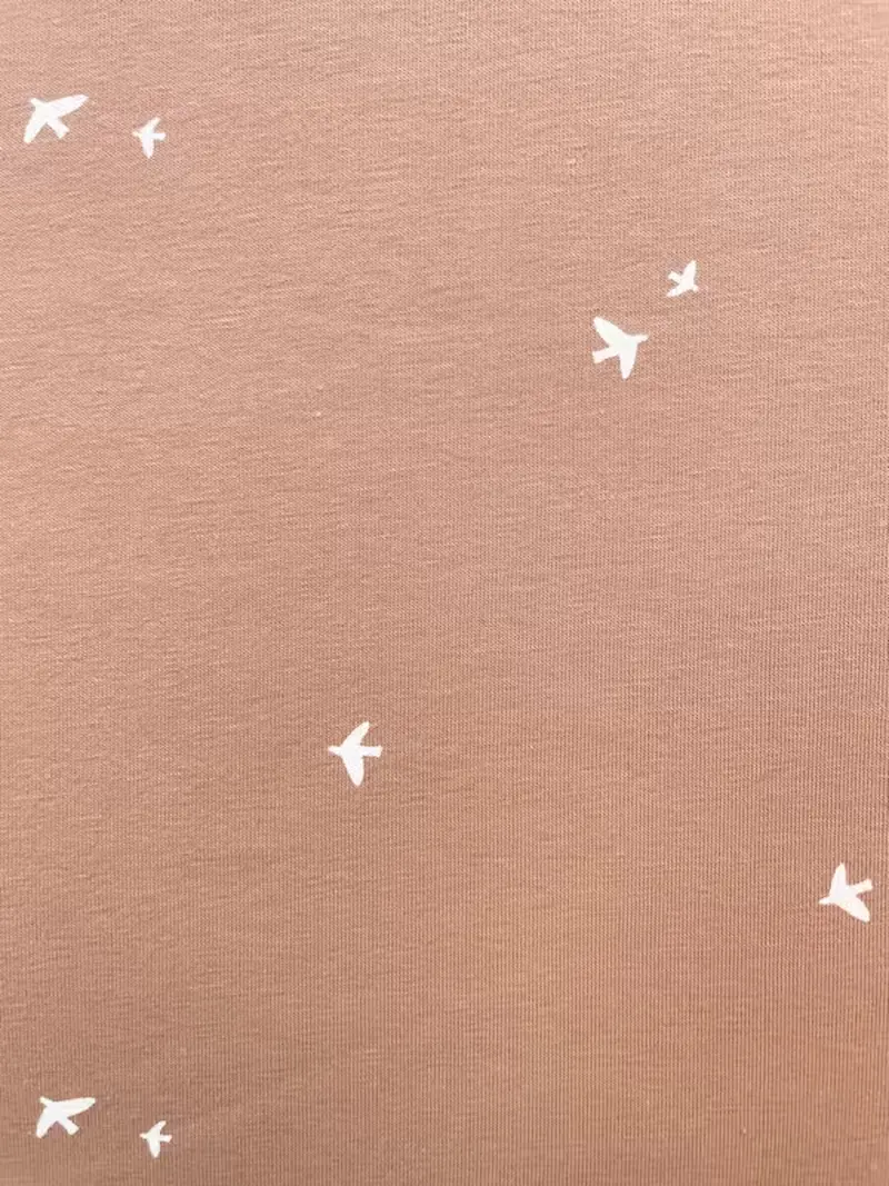 Elastischer Baumwolljersey in der Farbe Terracotta mit einem Muster aus kleinen, weißen Vögeln.