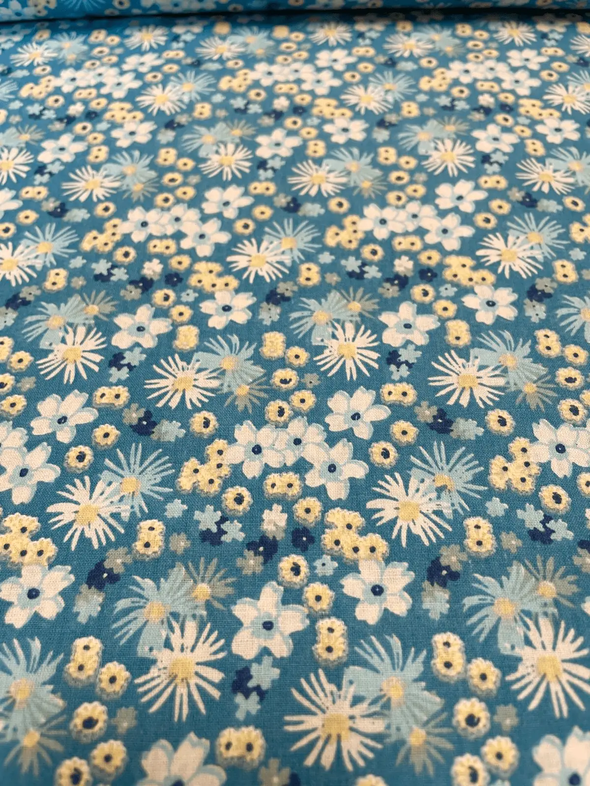 Hochwertiger Baumwollstoff als Meterware in Türkisblau mit dichtem, floralem Muster aus weißen, hellblauen und gelben Gänseblümchen und Blüten.
