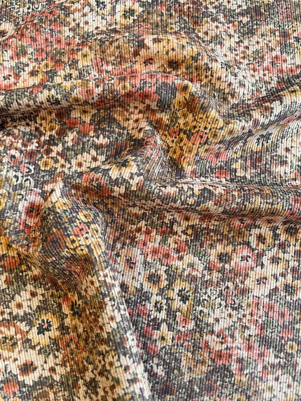 Gedrapieter Feincord-Jacquard Stoff als Meterware mit feinem Rippenmuster und herbstlichem Blumen-Print in Braun, Rosa und Ocker.