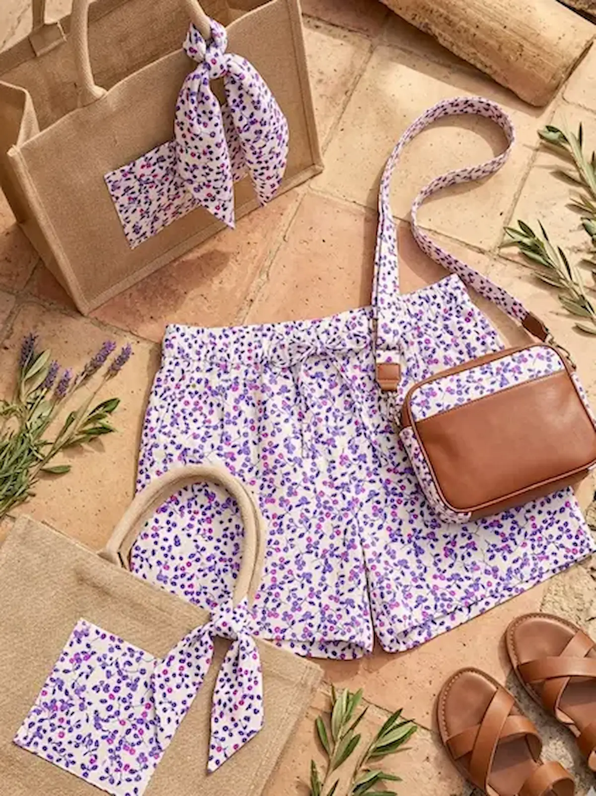 Sommerliches Set aus Bio-Baumwolle Popeline mit feinem Beerenmuster in Pink und Lila, bestehend aus Shorts und passenden Accessoires auf sonnigen Steinplatten.